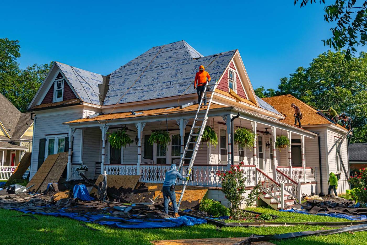 A roofer on a ladder replacing damaged sections of a residential roof