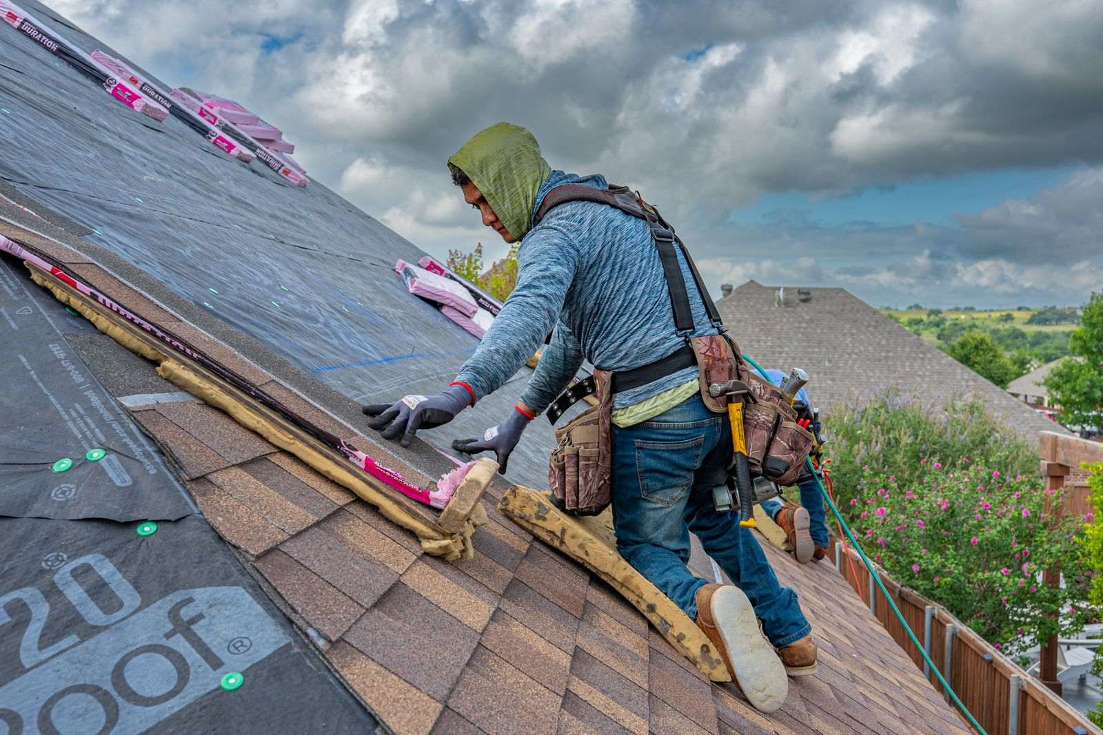 A roofer nailing asphalt shingles near the ridge of a sloped roof on a sunny day