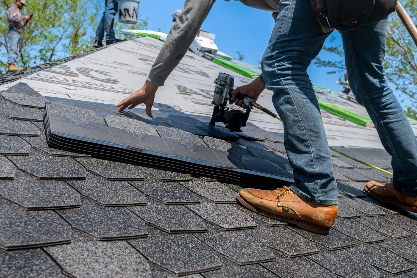 A roofer repairing a damaged section of a residential roof, shot close at roof level