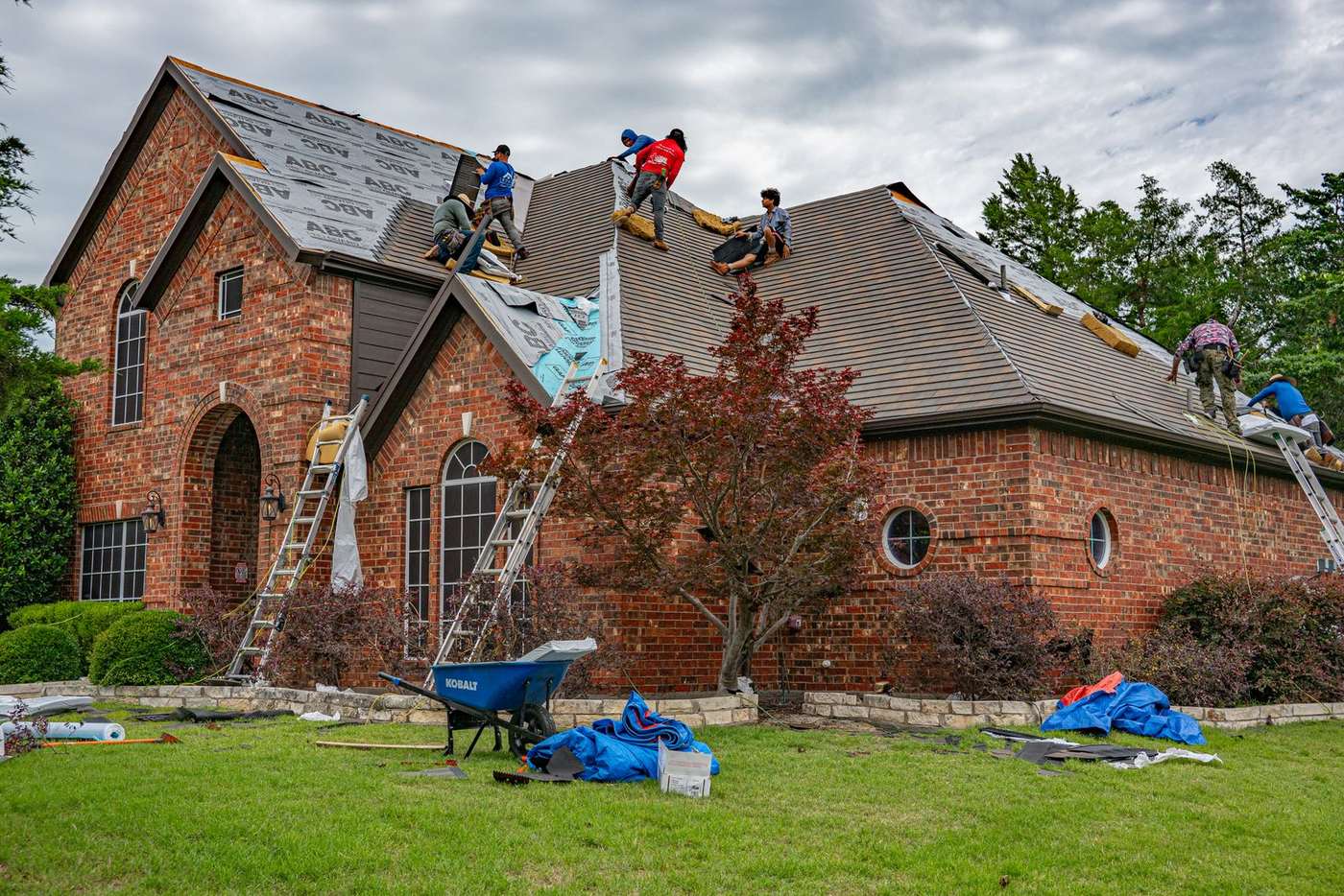 Two roofers replacing shingles on the roof of a brick house